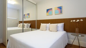 Habitación de hotel con una cama grande, una mesita de noche, un espejo y dos cuadros colgados en la pared.