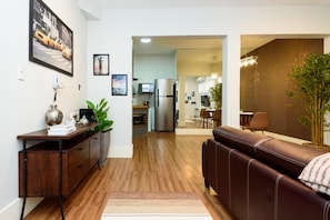 A modern living room with a wooden floor, a brown leather sofa, a desk with a plant, and a kitchen in the background. - 1 Minute From Ipanema Beach Vsc3 (Rio de Janeiro)