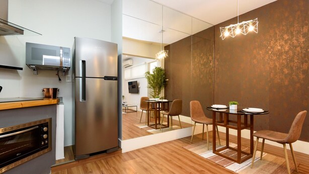 Una cocina moderna con microondas integrado, refrigerador de acero inoxidable y horno. Hay un comedor con mesa y sillas de madera.