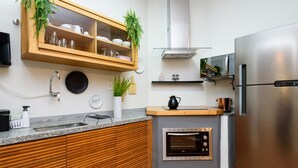 Una cocina moderna con armarios de madera, horno integrado, electrodomésticos de acero inoxidable y un mueble de vidrio con plantas decorativas.
