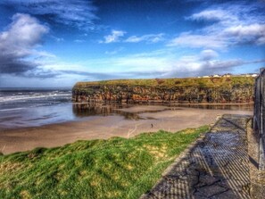 A coastal landscape with a grassy area, a stone pathway, and a cliff with vegetation.
