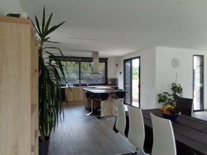 Enjoy meals at the dining table with four chairs, surrounded by a large potted plant and a bowl of fresh fruit.