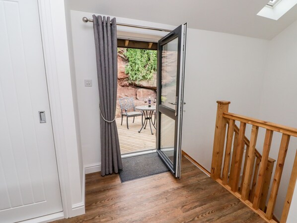 A room with a wooden floor, a white door, a glass door leading outside, and a wooden railing.