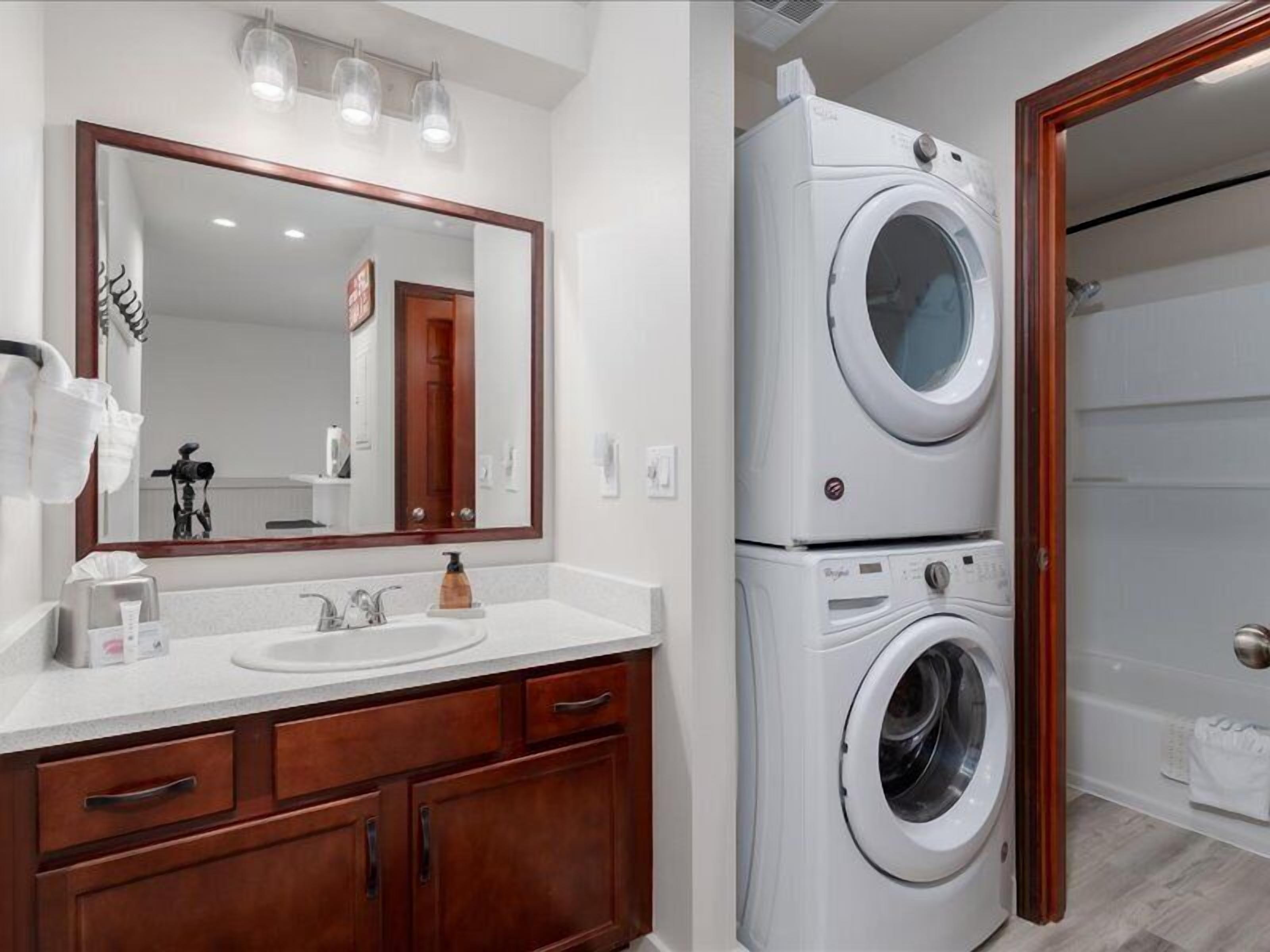 A bathroom with a double sink vanity, a large mirror, and stacked front-loading washers.