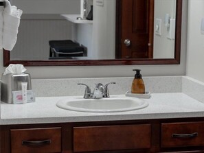 A bathroom with a white sink, two faucets, a mirror, a soap dispenser, and a tissue box.