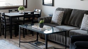 Een moderne woonkamer met een glazen salontafel, een grijze bank en een eethoek met een tafel en stoelen.