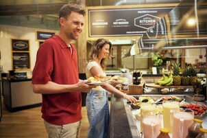 Zona de bufé con una variedad de opciones de comida y bebida, incluyendo frutas, sándwiches y batidos.
