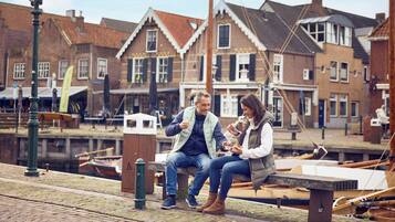 Una pareja sentada en un banco junto a un canal, con edificios tradicionales al fondo.