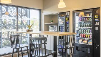 A cafe with a wooden table and four chairs, a vending machine with snacks, and a microwave.