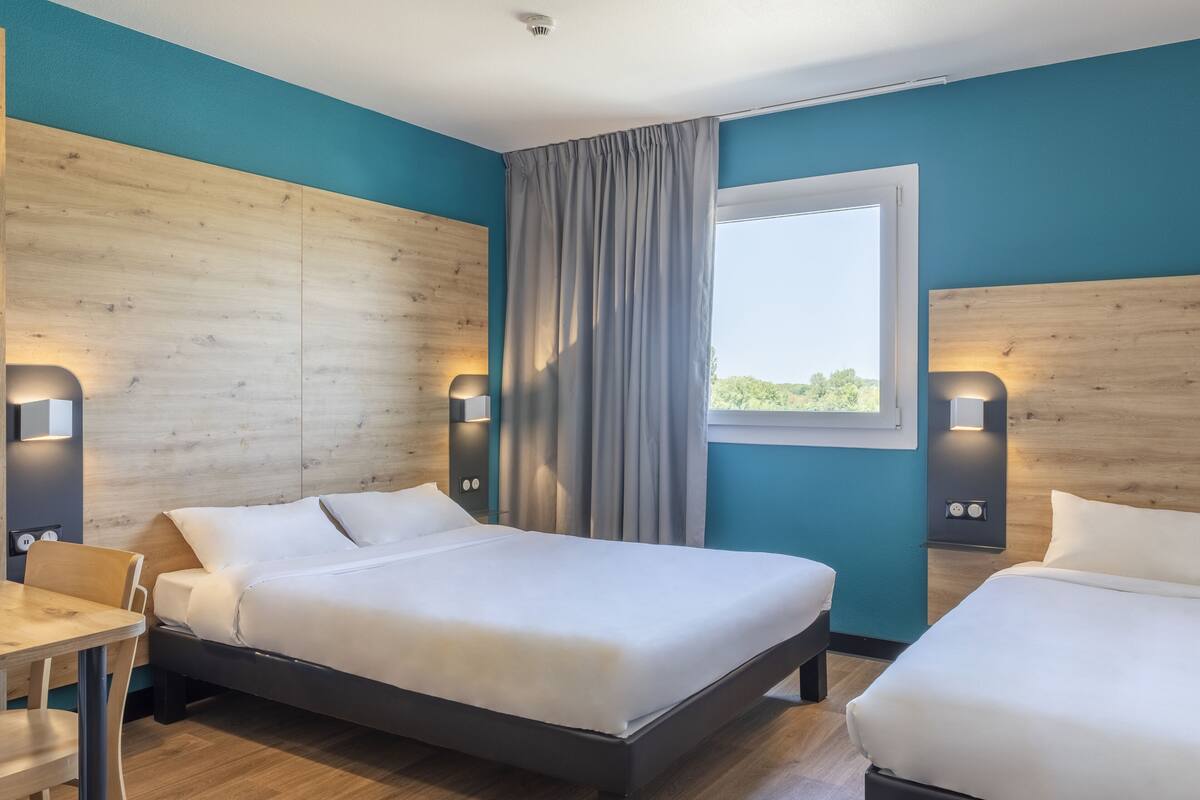 Ein Hotelzimmer mit zwei Betten, Holz-Kopfteilen, einem fenster mit Vorhängen und Wandleuchten.