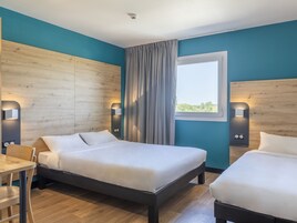 Habitación de hotel con dos camas, cabeceros de madera, una ventana con cortinas e iluminación en la pared.