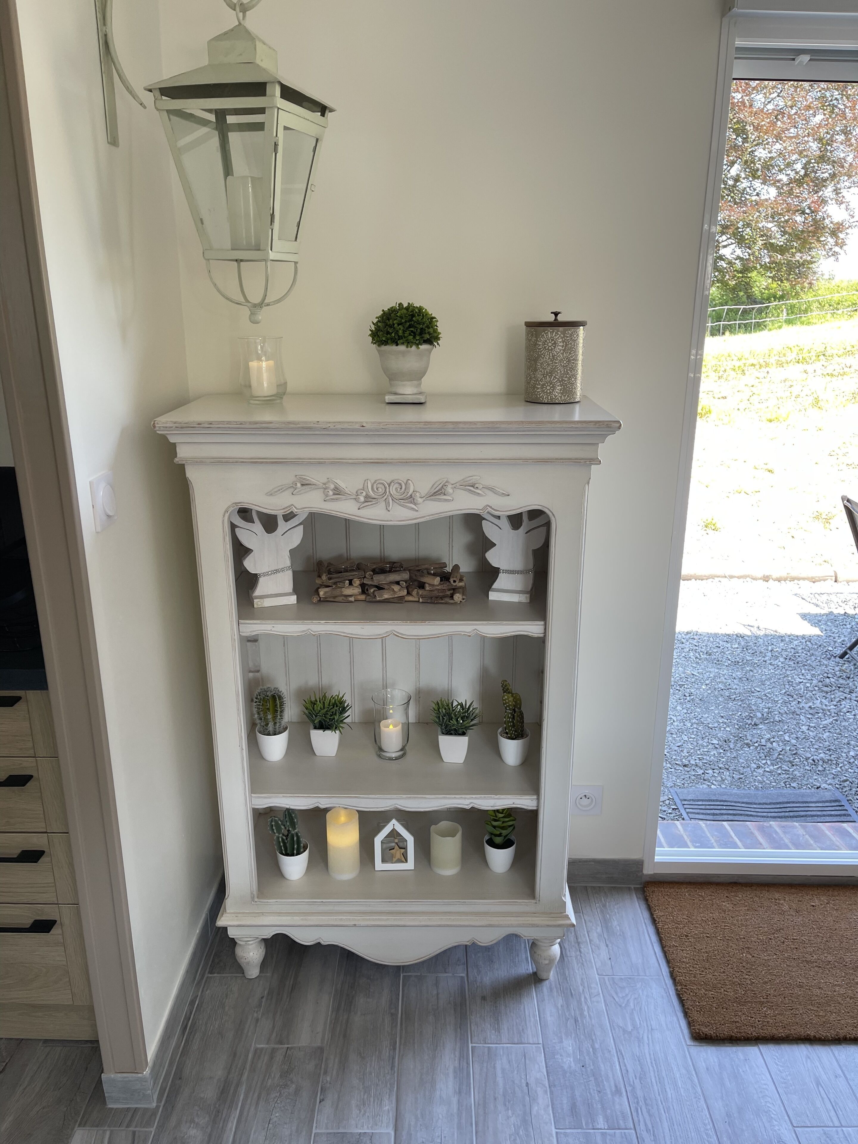 A white, ornate console table with a white lantern above it, a small potted plant, and a decorative container.