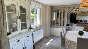 Ein Essbereich mit einem Tisch für zwei Personen, einer weißen Kommode mit Glastüren und Blick ins Freie durch ein Fenster.