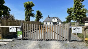 Ein verschlossener Eingang zu einem Anwesen mit Holzzaun, Schildern mit der Aufschrift 'Gîte au Pied d'Honneur' und 'Gîte à la Vie d'Enfleur' sowie einer Schotterauffahrt zu einem Haus.