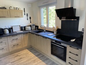 Une cuisine moderne avec des meubles en bois, un plan de travail noir, une hotte de cuisine Bosch, un grille-pain, une bouilloire et une machine à café.
