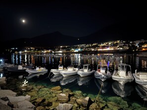 Ein beleuchteter Hafen bei Nacht mit vertäuten Booten, ruhigem Wasser und einer Stadtlandschaft im Hintergrund.