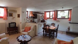 A cozy living room with a sofa, a dining table with chairs, a television, and a kitchen area with a stove and cabinets. - APARTMENT IN DORGALI, COMFORT AND RELAX GARDEN (Dorgali)