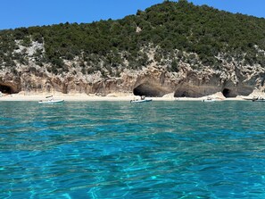 A coastal scene with clear turquoise waters, boats, and a rocky cliff with a cave entrance.
