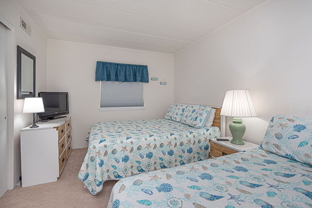 Une chambre avec deux lits, une télévision, une commode et une lampe.