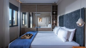 A modern hotel room with a large bed, a wooden headboard, a bedside table, and a window with curtains. - Archipelagos Apt with Unique Sea & Old Port View in the City Center (Heraklion)