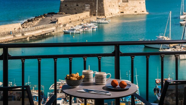 A balcony with a table set for breakfast, overlooking a harbor with boats and a historic fort. - Archipelagos Apt with Unique Sea & Old Port View in the City Center (Heraklion)