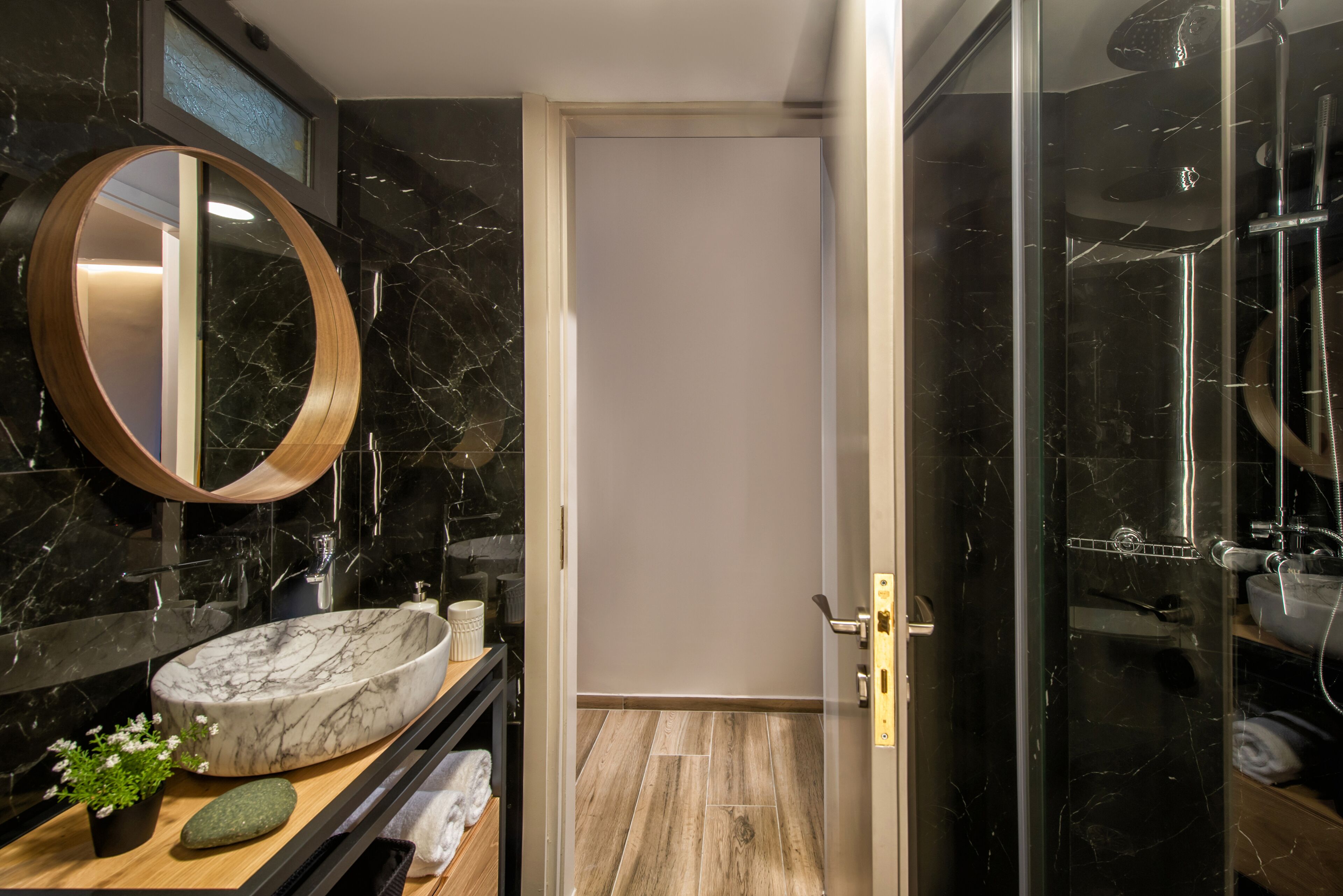 A modern bathroom with a marble sink, a round mirror, and a glass-enclosed shower.