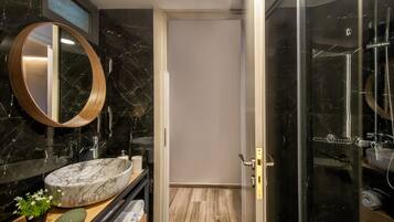 A modern bathroom with a marble sink, a round mirror, and a glass-enclosed shower.