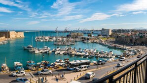 A coastal marina with boats, a fortified structure, and a road with vehicles. - Archipelagos Apt with Unique Sea & Old Port View in the City Center (Heraklion)