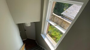 A staircase with a wooden handrail leading to a landing with a window overlooking a garden.