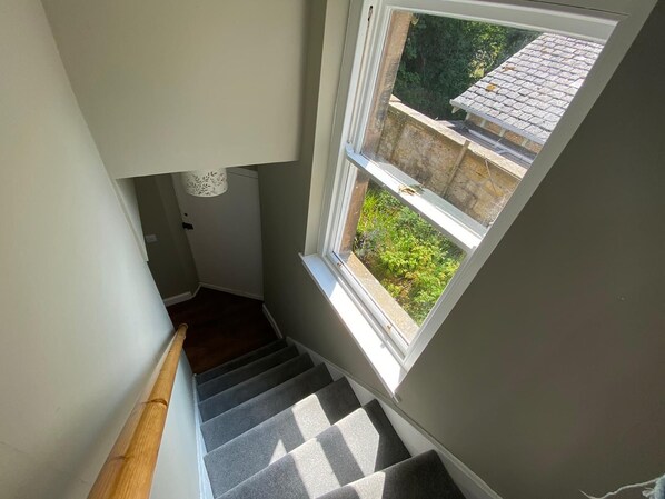 Una escalera con barandilla de madera que conduce a un rellano con ventana con vistas a un jardín.