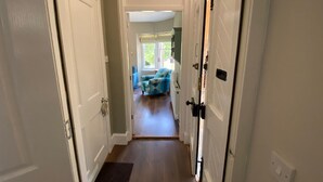 A hallway leading to a room with a blue patterned sofa and a window with blinds.