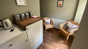 A compact kitchen with a wooden countertop, tea and coffee containers, a kettle, wicker chairs, and a radiator.