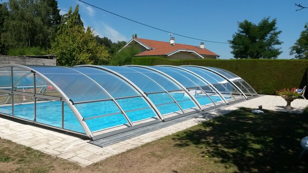 A covered swimming pool with a transparent roof, surrounded by a paved deck and a hedge. - Un Lieu Bucolique, Idéal Pour se Ressourcer (Beauzac)