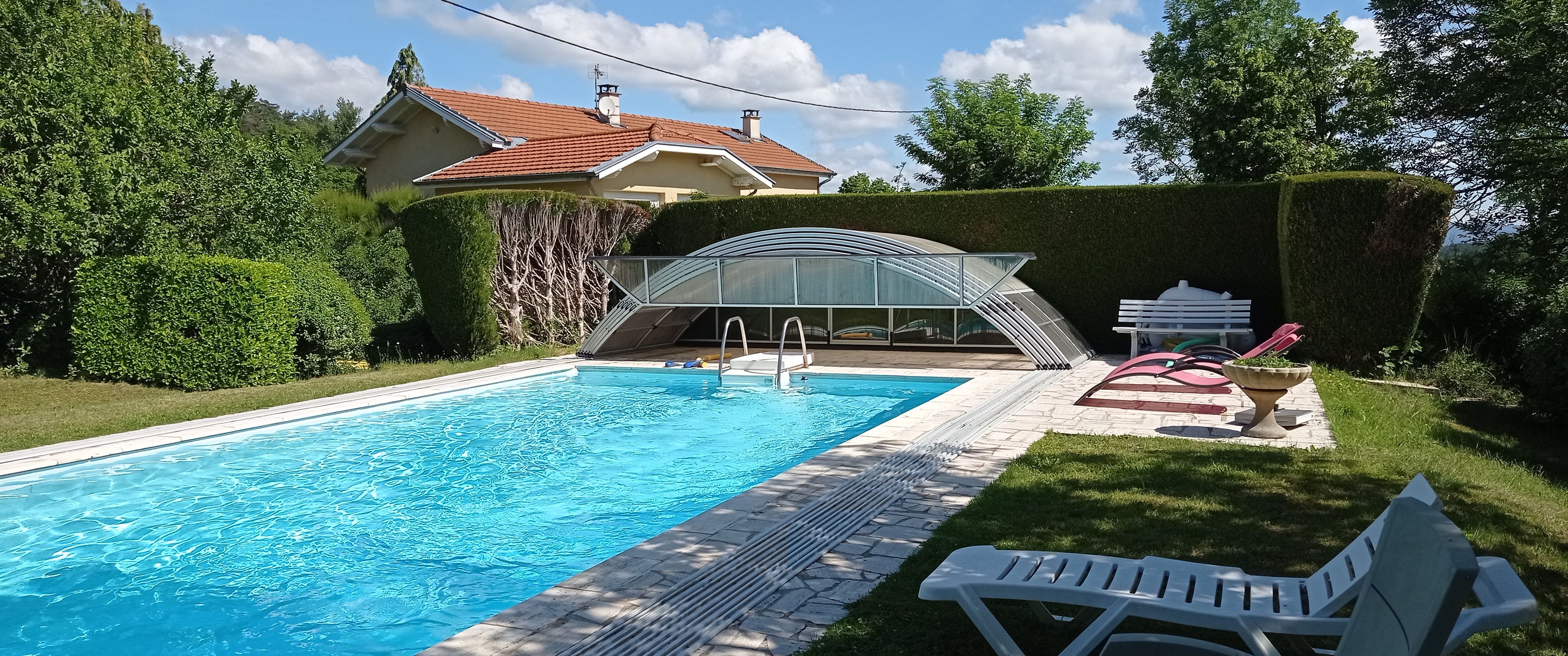 A swimming pool with a glass enclosure, surrounded by a well-maintained lawn and hedges.