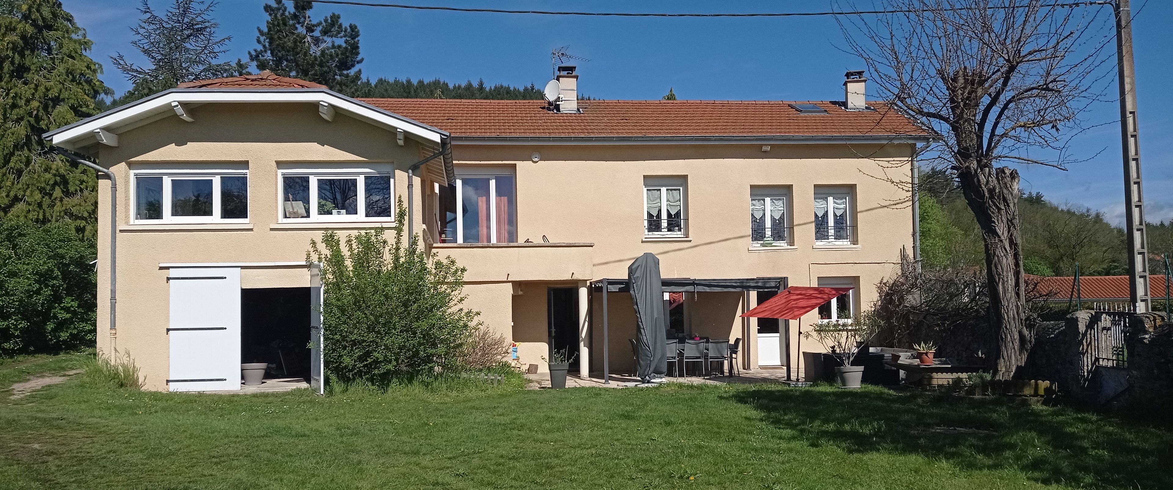 Una casa de dues plantes amb façana beix, teulada de rajoles vermelles i zona de terrassa coberta.