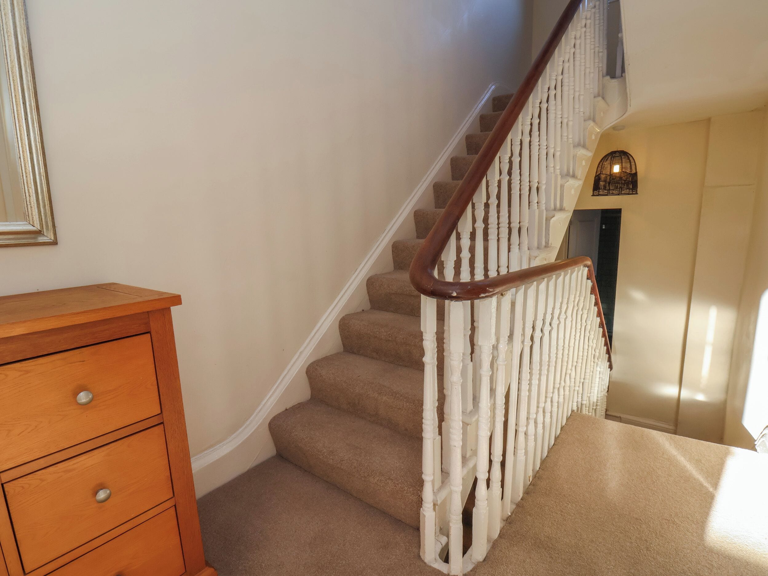 A staircase with a wooden handrail and beige carpeted steps.