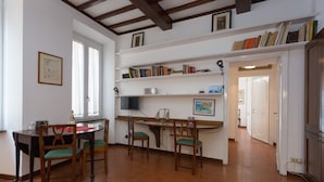 Un comedor con una mesa y sillas, una estantería y una zona de cocina con armarios.