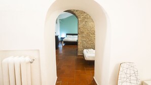 A hallway leading to a bedroom with a stone wall, a radiator, and a bed with white linens. - Campo de Fiori Grotto Apartment (Roma)