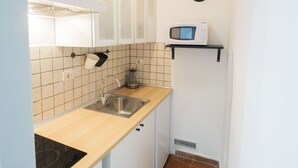 A compact kitchen with white cabinets, a stainless steel sink, a microwave on a shelf, and a clock on the wall. - Campo de Fiori Grotto Apartment (Roma)