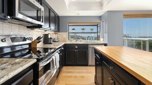 A modern kitchen with black cabinets, stainless steel appliances, a wooden countertop, and a window with a view of the city. - Vista Pacific- Del Mar Rental with Ocean Views, Pool, A/C & Walkable Dining (Del Mar)