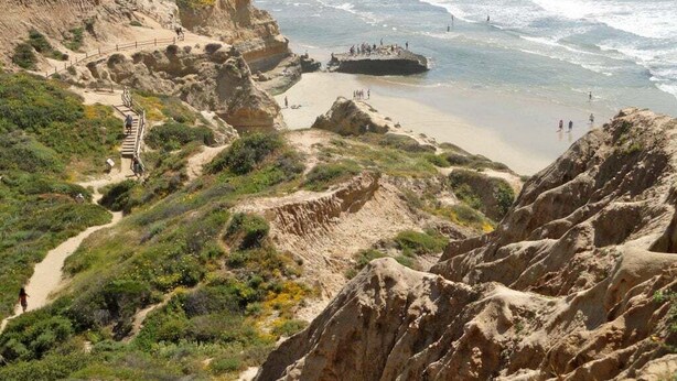 A coastal landscape with a rocky cliff, a sandy beach, and a path leading to a viewpoint overlooking the ocean. - Vista Pacific- Del Mar Rental with Ocean Views, Pool, A/C & Walkable Dining (Del Mar)