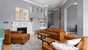 A living room with a fireplace, leather sofas, a coffee table, and a large wall art piece. - Vista Pacific- Del Mar Rental with Ocean Views, Pool, A/C & Walkable Dining (Del Mar)
