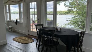 Zona pranzo con tavolo e sedie, ampie finestre vista lago e un elemento decorativo rustico sopra le finestre.