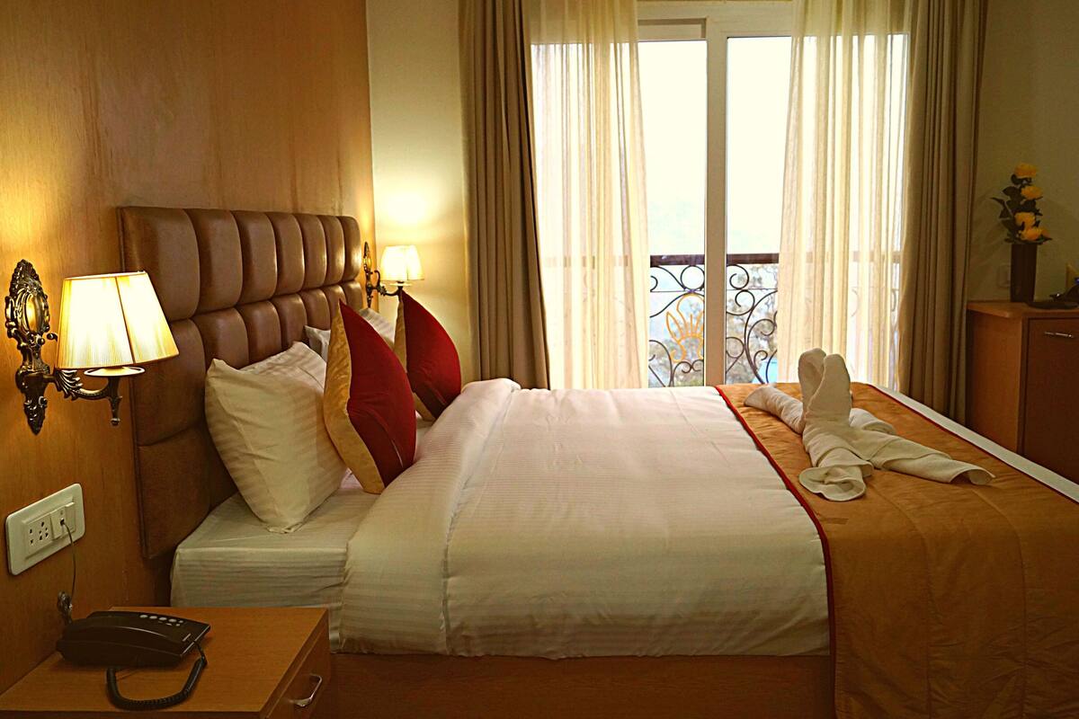 A hotel room with a bed, bedside lamps, a telephone, and a view of the outside through a window.