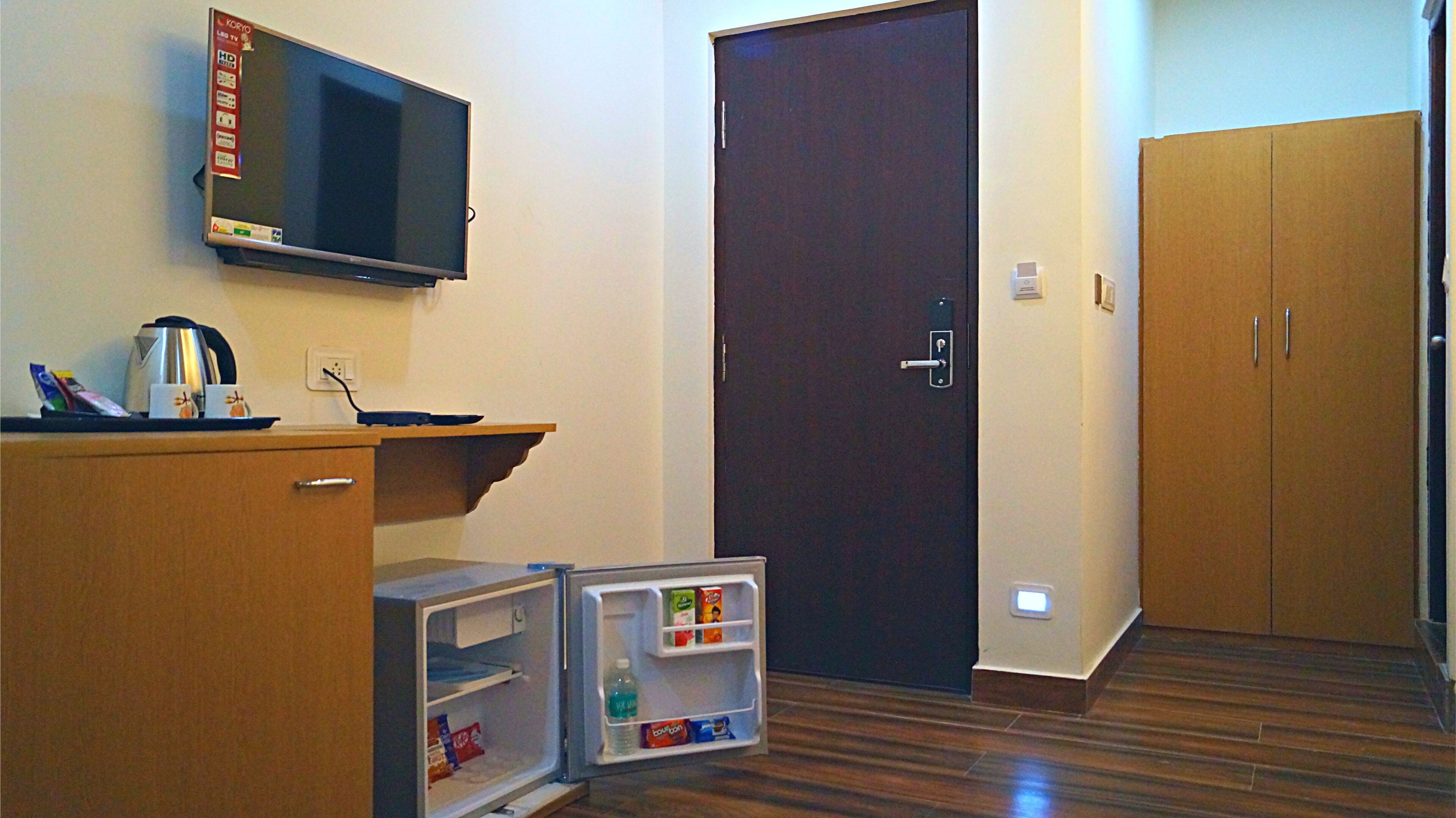 A hotel room with a TV, a mini-fridge, a coffee maker, a wooden wardrobe, and a door.