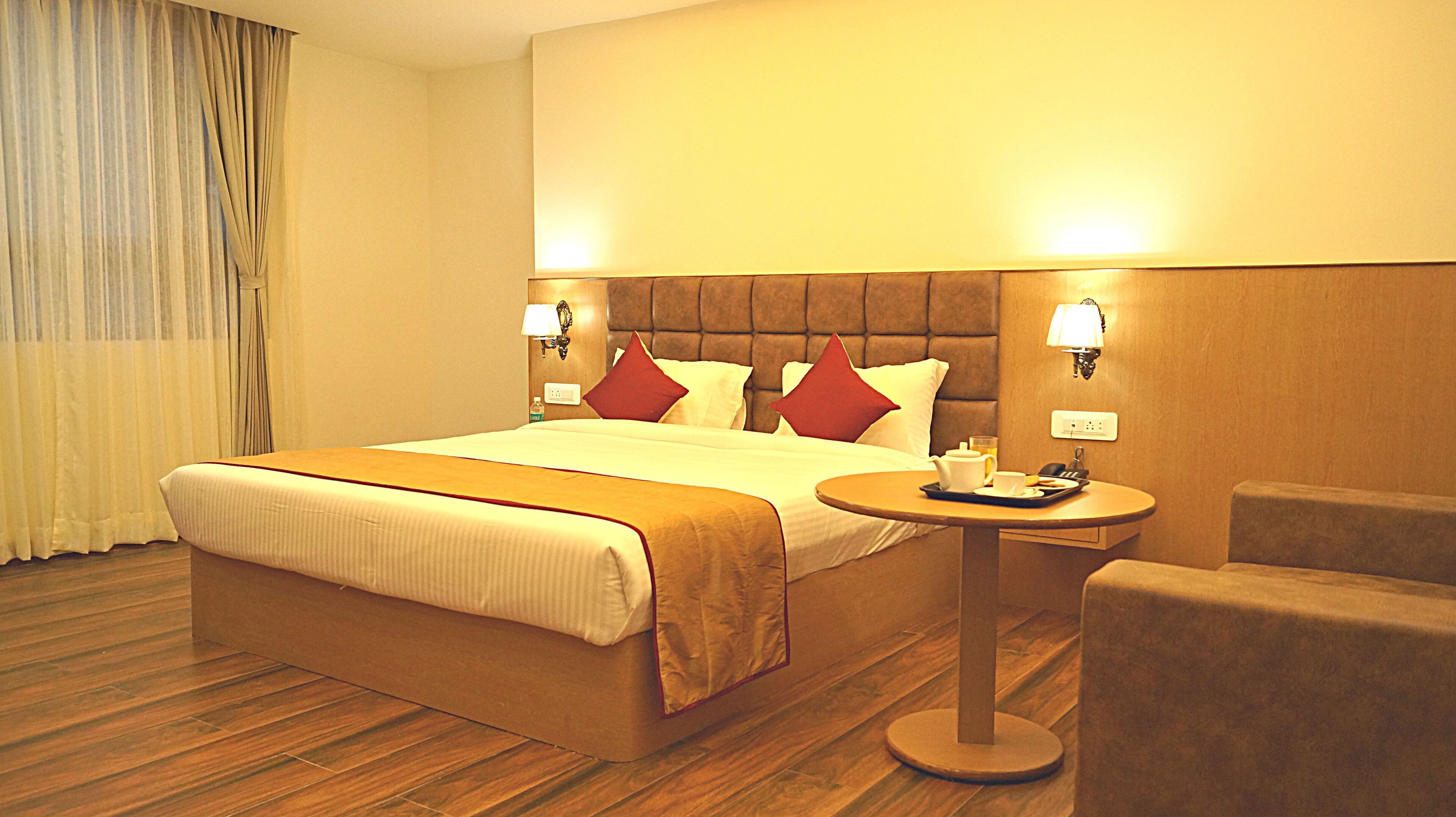 A hotel room with a large bed, two bedside lamps, a small table with a tray, and a chair.
