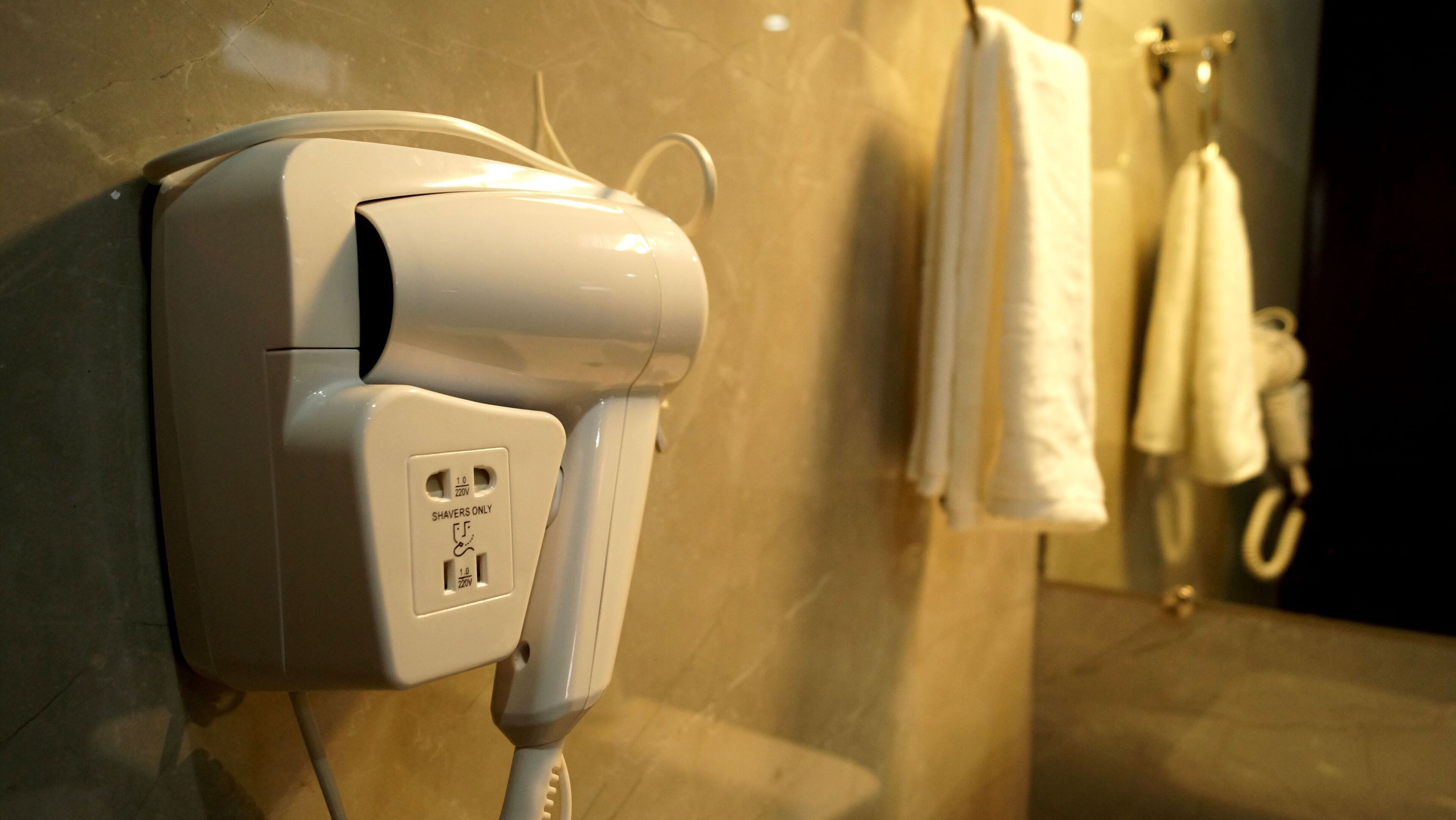 A hairdryer mounted on a wall in a bathroom with towels hanging nearby.