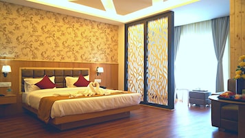Habitación de hotel con una cama grande, cabecera de madera, papel tapiz floral y vistas a través de un separador decorativo.