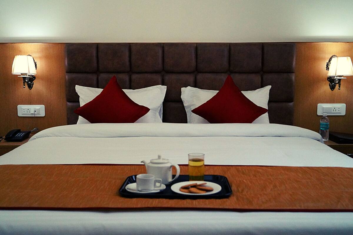 A hotel room with a large bed, two bedside lamps, a telephone, and a tray with a cup, a glass, and cookies.