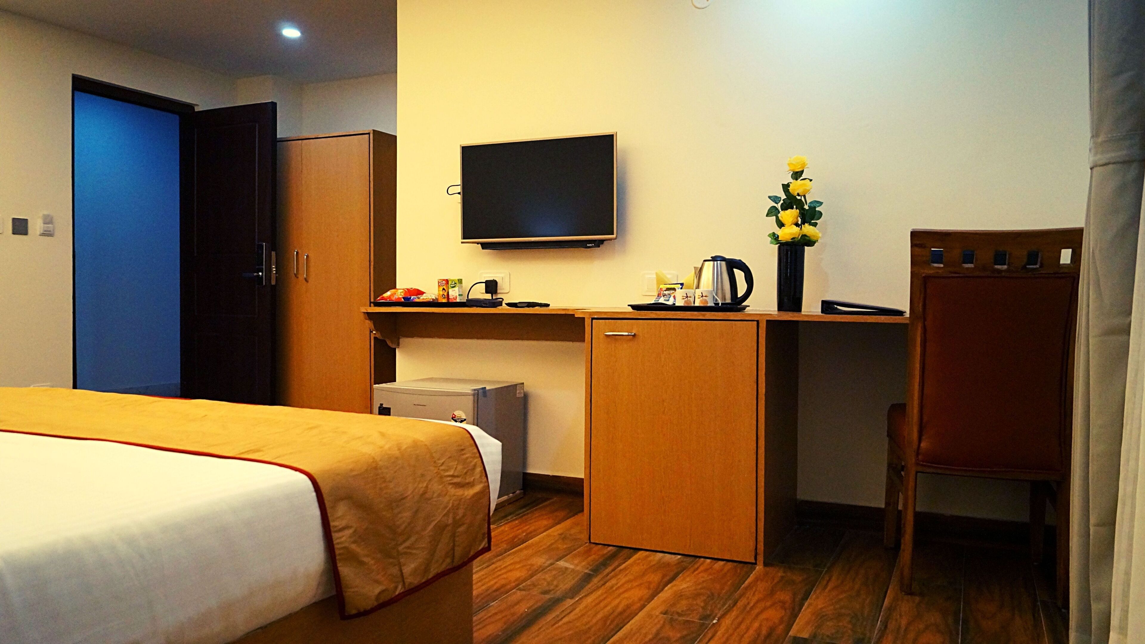 A hotel room with a bed, a desk, a television, a small refrigerator, and a chair.